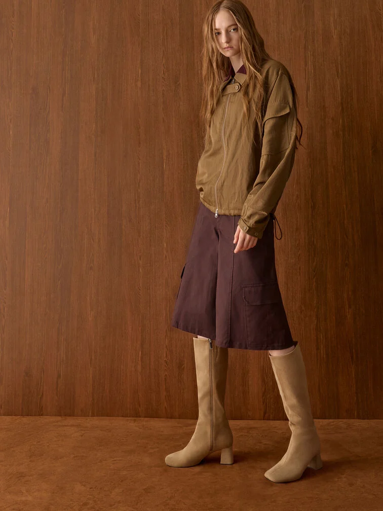 Sand square-toe knee-high boots paired with relaxed dark-brown Bermuda shorts for contrast.