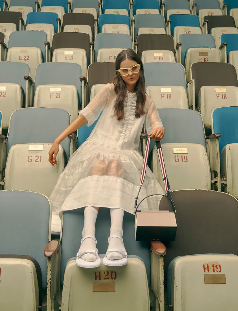 A model in velcro strap sandals, a top handle box bag and printed geometric frame sunglasses.