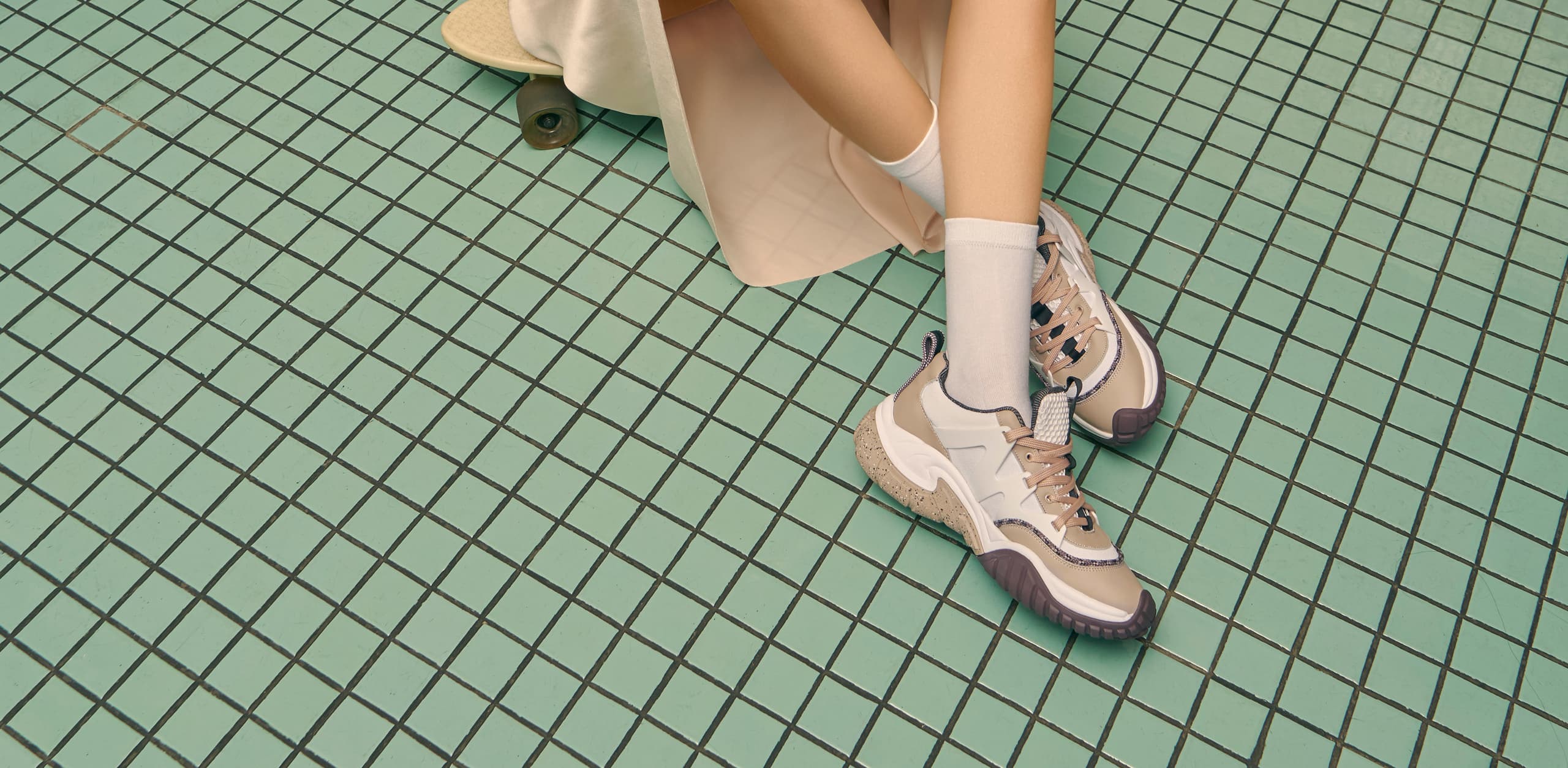 A pair of mesh chunky sneakers in nude pictured against green square tiles – sitting.