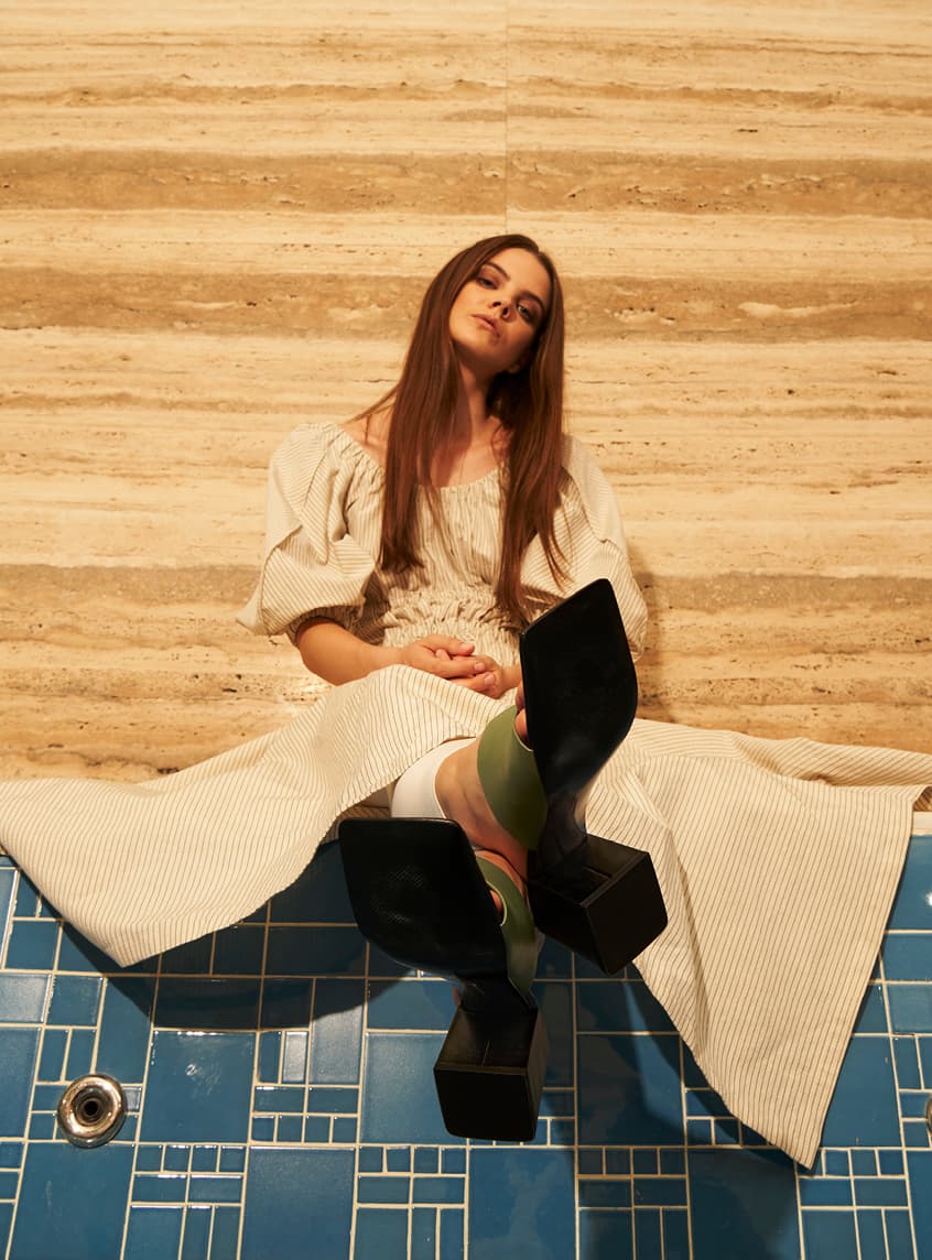 A model wearing a puff sleeve dress with square toe mules – sitting down