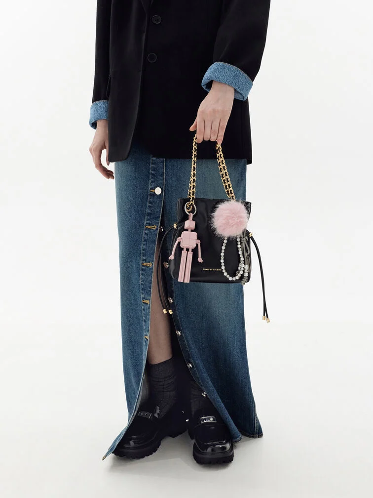 Multiple bag charms of varying sizes and textures clipped onto each side of the bag’s handle.