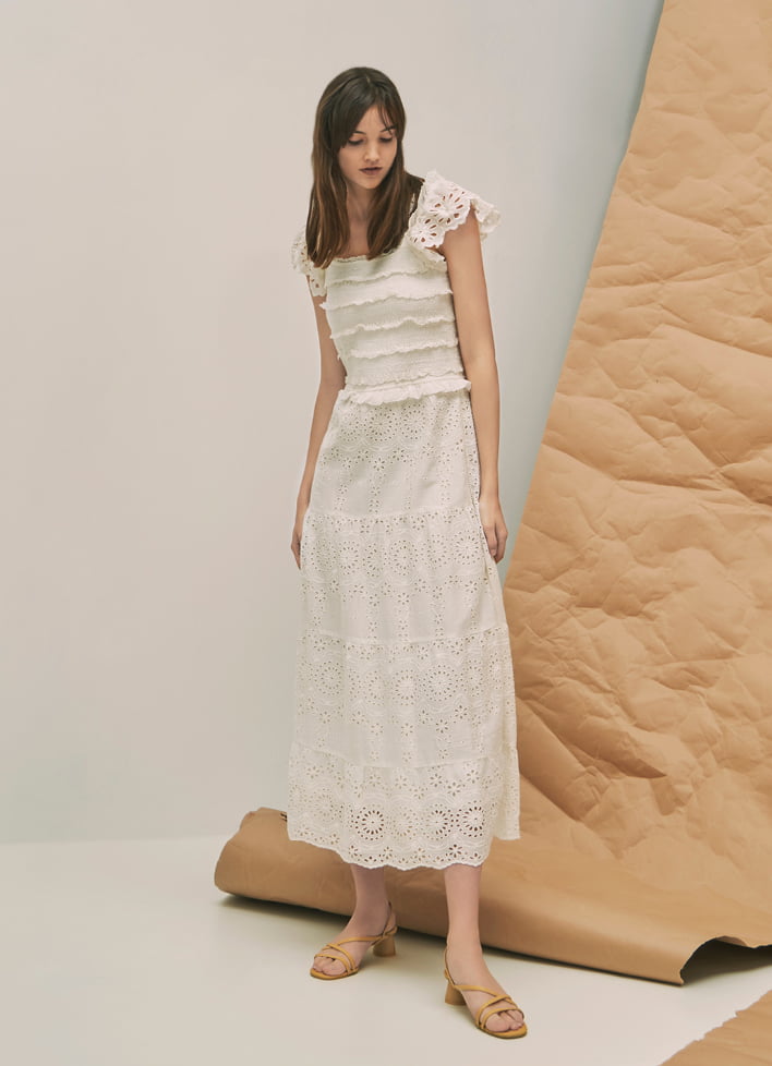 A model wearing a maxi white dress with strappy cylindrical heel sandals.